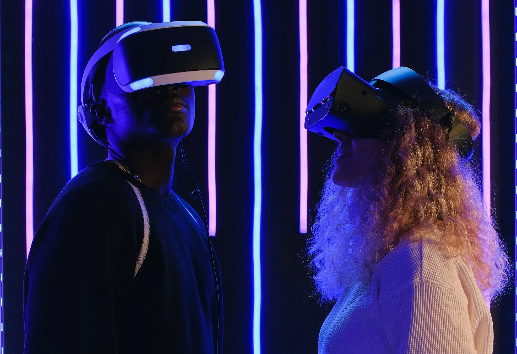 Two people standing next to neon night lights wearing VR goggles