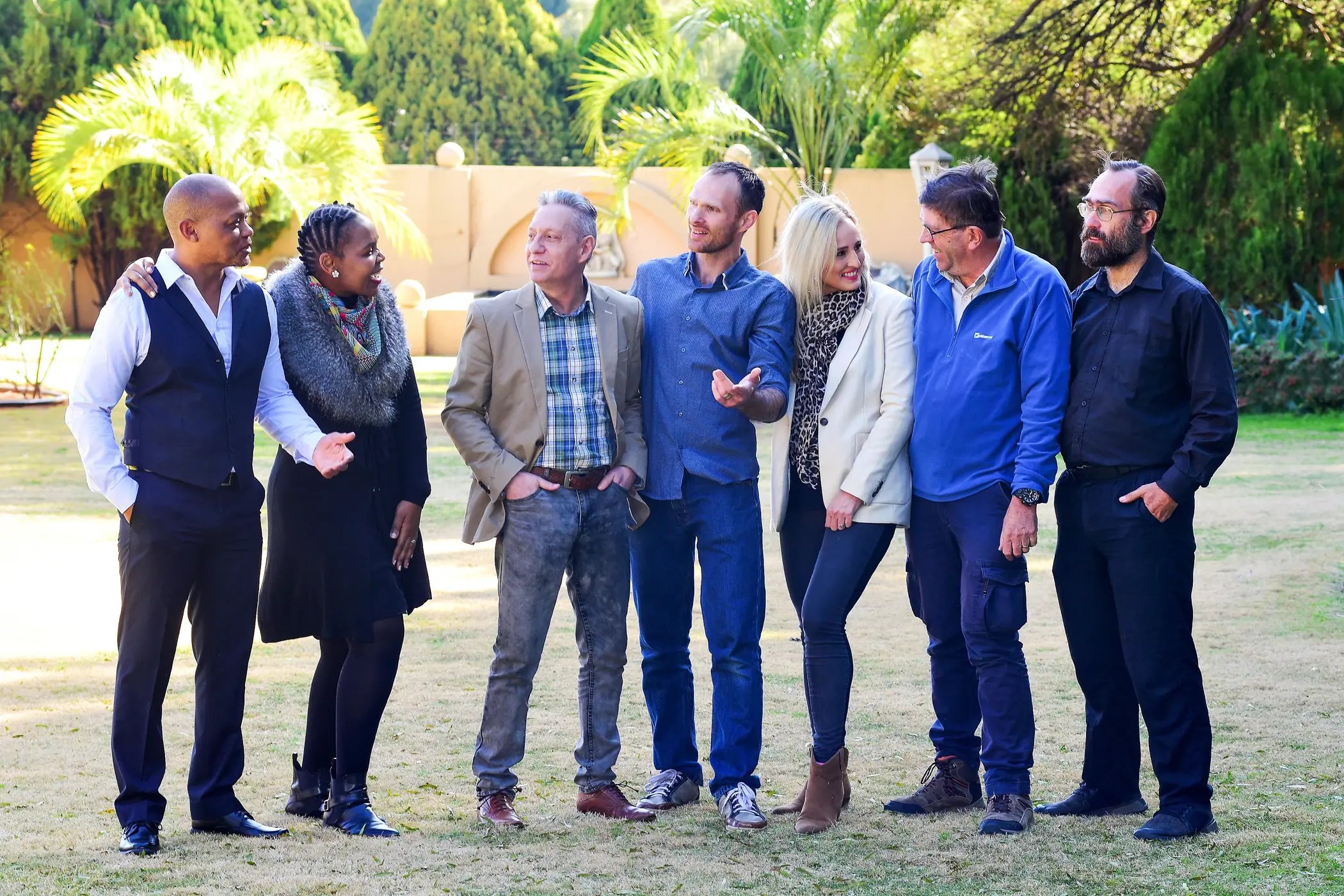 Founders talking together on a lawn at a networking gathering, palms and a garden wall behind them.